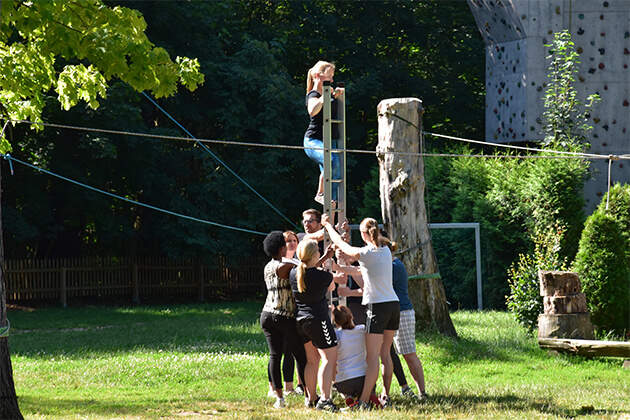 Eine Gruppe von Menschen halten eine Leiter während eine Person hinaufklettert. Eine Gruppe von Menschen halten eine Leiter während eine Person hinaufklettert.