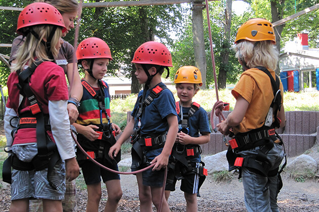 Eine Gruppe von Kindern wird für den Kletterpark von einer Mitarbeiterin vorbereitet Eine Gruppe von Kindern wird für den Kletterpark von einer Mitarbeiterin vorbereitet